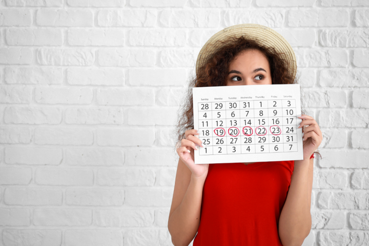 Woman with monthly calendar in hand in front of a white wall