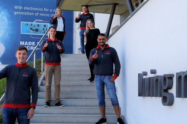 Four trainees and two employees stand on a staircase in front of the company building of Micro-Hybrid