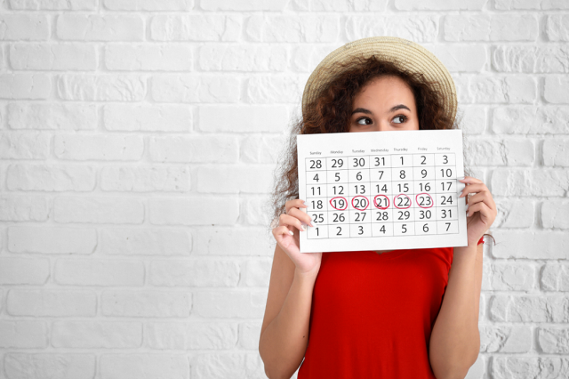 Frau mit Monatskalender in der Hand vor weißer Wand