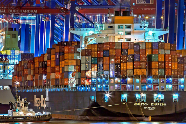 Large cargo ship in industrial port at night with a small ship in the foreground